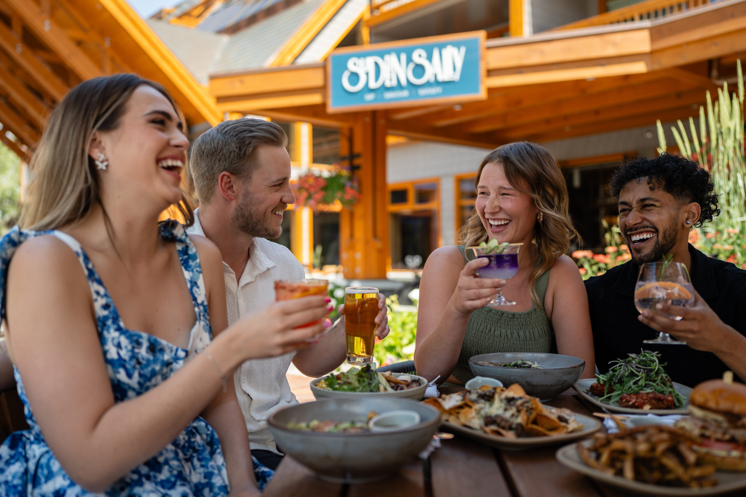 Two couples enjoying food and cocktails on the Sudden Sally patio in Banff